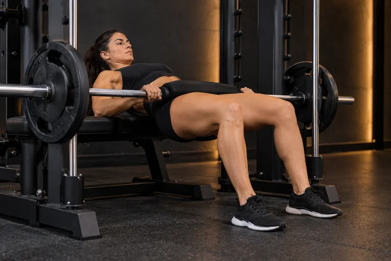 Demostración de hip thrust en multipower en un gimnasio oscuro